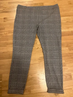 Rutiga kostymbyxor från Cellbes - Snygga kostymbyxor från Cellbes i svartvitt rutigt mönster. Byxorna har smal passform, klassisk midja och uppvikta benslut. Perfekta för dig som gillar stilrena och trendiga plagg. Materialet känns mjukt och stretchigt.
