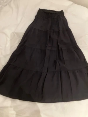 Svart långkjol med volanger storlek 146 i mycket bra skick. - Säljer en svart långkjol med bred resår i midjan och flera volanglager. Kjolen har en luftig och flowy passform, perfekt för dig som gillar en avslappnad men ändå stilren look. Material 78% viscose 22% polyamid, i mycket bra skick.