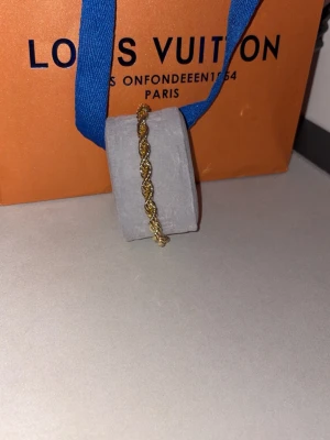 Guldigt tvinnat armband  - Snyggt armband i guldfärgad metall med tvinnad kedjedesign. Armbandet har en elegant och stilren look som passar perfekt till din outfit.