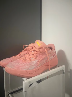 Rosa basketskor från Puma ! - Säljer ett par snygga rosa sneakers från Puma med gula loggor på plösen. Skorna har en sportig design med lågt skaft, snörning och mönstrad ovandel i textil och syntet. Perfekta för dig som vill sticka ut med färg i baskethallen, gymmet eller i vardagen.