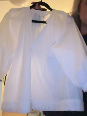 H&M blus - Stilren vit blus med v-ringning och puffiga långärmar. Blusen har en lös passform och är tillverkad i ett lätt tyg som ger en luftig känsla. Perfekt att matcha med jeans eller kjol för en trendig look