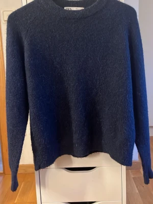 Mörkblå fluffig stickad tröja Zara - Mysig mörkblå stickad tröja från Zara med fluffig yta. Tröjan har rund halsringning, långa ärmar och en avslappnad passform. Använd fåtal gånger!