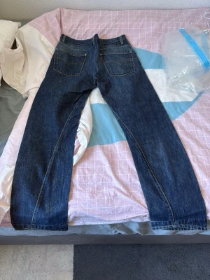 Mörkblå raka jeans med bakfickor - Säljer ett par mörkblå jeans med raka ben och två stora bakfickor. Klassisk femficksmodell med kontrastsömmar och normal midja. Passar perfekt till en avslappnad stil och är ett måste i garderoben.