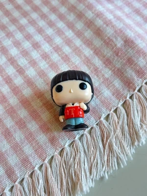 Stranger Things kinder joy will Funko Pop minifigur svart hår - Säljer en liten Stranger Things Will Funko Pop Kinder Joy minifigur med svart hår, stora svarta ögon och röd jacka. Figuren har blå byxor och svarta skor. Tillverkad i plast och har typisk Funko-stil med stort huvud och små detaljer.