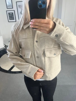Beige kappa/overshirt - Beige overshirt/kappa från Zara. Den har en krage och stora bröstfickor med lock och tryckknappar. Rak passform och långa ärmar med knapp vid ärmslut. Materialet är lite mjukt och lite tjockare, perfekt för vår och höst väder. Passar till både jeans och kjol. Aldrig använd!