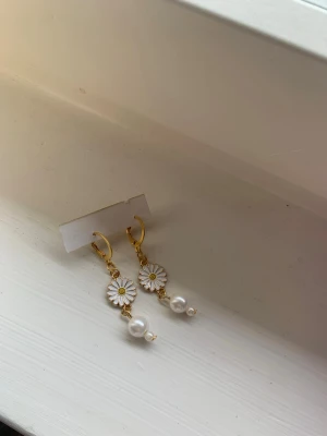 Guldörhängen med blommor och pärlor - Snygga örhängen i guldton med vita emaljblommor och hängande pärlor. Blommorna har en liten gul detalj i mitten och örhängena har en elegant, droppformad design. Perfekta för att ge din look en söt och trendig touch.