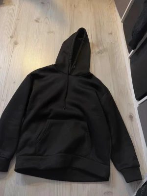 Svart hoodie från SHEIN med huva - En klassisk svart hoodie från SHEIN med stor känguruficka framtill och justerbar huva med dragsko. 