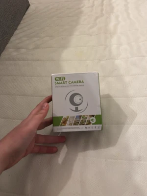 WiFi Smart Camera övervakningskamera - Säljer en WiFi Smart Camera som är perfekt för övervakning hemma. Kameran är vit och levereras i originalförpackning med grön och vit design. Enkel att installera och koppla upp till ditt nätverk för smidig övervakning via mobilen.