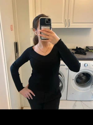 Svart stickad tröja med v-ringning - Snygg svart stickad tröja med djup v-ringning och lång ärm. Tröjan har en figurnära passform och är tillverkad i ett mjukt, stretchigt material som sitter bekvämt på kroppen. Perfekt att matcha med jeans eller kjol för en stilren look.