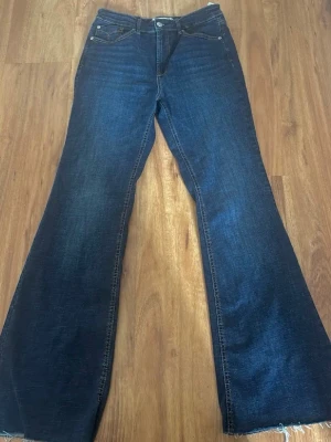 Mörkblå bootcut jeans Stradivarius - Säljer ett par mörkblå bootcut jeans från Stradivarius i storlek 42. Jeansen har klassisk femficksdesign, hög midja och råa kanter nertill. Tillverkade i stretchig denim för skön passform och snygg siluett. Jag är 1.68 cm så de är snäppet långa på mig utan skor. Perfekta på dig som är mellan 168-170 cm.