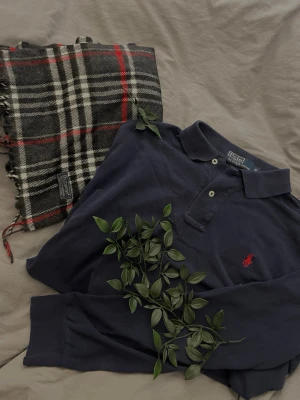 Mörkblå polotopp från Polo Ralph Lauren - Klassisk mörkblå polotopp från Polo Ralph Lauren med röd broderad logga på bröstet. Tidlös design med krage och knappar framtill. Perfekt till jeans eller kjol för en clean och stilren look.