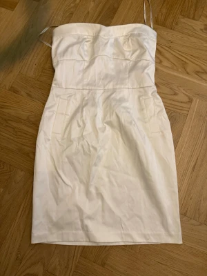 Vit kort klänning med smala band - Säljer en stilren vit kort klänning med smala axelband och figurnära passform. Klänningen har en enkel design utan mönster och är perfekt för sommarens alla tillfällen. Tillverkad i ett mjukt material som känns bekvämt mot huden.