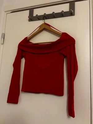 Röd offshoulder topp - Trendig röd offshoulder topp med långa ärmar och bred krage som vilar över axlarna. Snygg croppad passform som passar perfekt till både jeans och kjol. Materialet känns mjukt och stretchigt, vilket gör toppen bekväm att bära. Aldrig använt eftersom jag ej tar på croppat. 