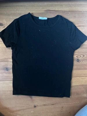 Svart basic t-shirt i bomull - En enkel tight svart t-shirt med rund hals och korta ärmar. Tillverkad i mjuk bomull, perfekt för en clean och stilren look. Passar till allt och är ett måste i garderoben.