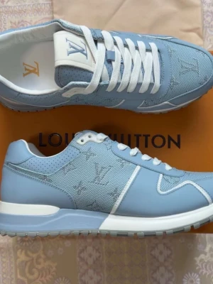 Blå Louis Vuitton sneakers - Snygga ljusblå sneakers från Louis Vuitton med klassiskt LV-monogram i tyget. Skorna har vita detaljer, perforerade partier och vita skosnören. Yttermaterialet är en mix av läder och textil för en exklusiv känsla och modern look.