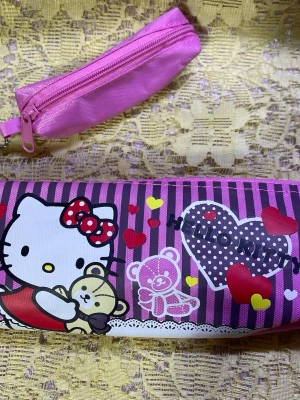 Hello Kitty rosa pennfodral - Säljer ett gulligt rosa pennfodral med Hello Kitty-motiv, hjärtan och nallebjörn. Fodralet har dragkedja och är gjort i ett tåligt tygmaterial med lila och rosa ränder. Perfekt för att förvara pennor och småprylar i väskan.