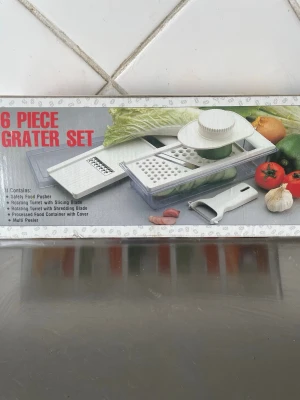 6-delars rivjärnset för köket - Säljer ett 6-delars rivjärnset i vitt plast och metall. Setet innehåller olika rivjärn, matbehållare med lock, säkerhetshållare och skalare. Perfekt för att riva, skiva och strimla grönsaker och frukt. Allt du behöver för att fixa sallad eller matlagning snabbt.