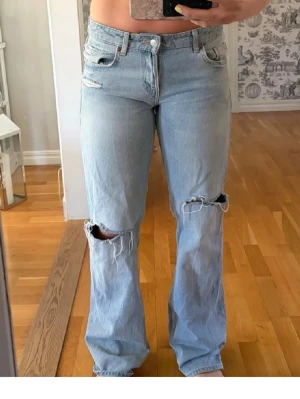 Ljusblå slitna jeans från Zara - Ljusblå jeans med slitningar vid knäna. Klassisk femficksmodell med hög midja och dragkedja. Jeansen har en avslappnad passform och är tillverkade i denim. Perfekta för en casual och trendig look. Storlek 42 men passar också 38 eftersom den är liten i storleken.
