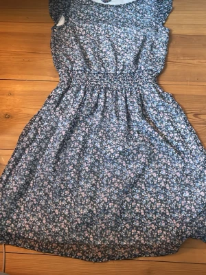 Blommig klänning med resårmidja - Söt klänning med småblommigt mönster i blått, rosa och vitt. Klänningen har resår i midjan för en bekväm passform och korta ärmar. Mjukt o lent material som är skönt att ha på sig. Inte genomskinlig. Perfekt sommarklänning till midsommar/skolavslutningar osv. Strl 158