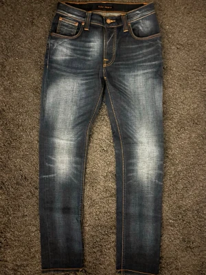 Nudie Thin Finn Broken Orange W31 L34 (Unika) - Unika Mörkblå Nudie Thin Finn "Broken Orange" med snygg stretch och klassiska orange sömmar. Premium denim i en sjukt snygg tvätt. 🧵 Nudie Jeans - Thin Finn (Broken Orange) 📏 W31 L34. Slim fit. 🧩 98% bomull / 2% elastan. Premium stretch-denim. 📐 Mått: Midja 37cm, Längd 103cm, Benslut 16cm, Lår 24cm. ✅ 9/10 – Mycket fint skick, mjuk premium denim, bilderna säger sitt.  ✨ Orange broderi på bakfickor, läderpatch, bio-bomull. 💰 Ca 1700 kr. ‼️Skickas snabbt‼️