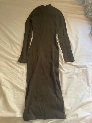 Mörkgrön långärmad långklänning - Långklänning i mörkgrön ton med lång ärm och hög hals. Klänningen har en kroppsnära passform och är tillverkad i ett mjukt, stretchigt material som ger en smickrande siluett. Perfekt för dig som gillar minimalistisk och stilren design.