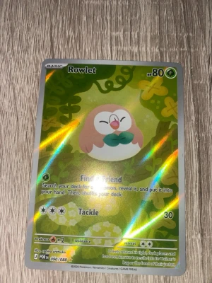 Pokémonkort Rowlet holo - Säljer ett holografiskt Pokémonkort med Rowlet-motiv från serien Sword & Shield. Kortet har gröna och gula färger med glittrande effekt och visar Rowlet i en tecknad skogsmiljö. Perfekt för samlare eller Pokémonfans!