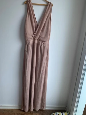 Dry Lake lång klänning stl S - Säljer en elegant långklänning i brunt / beige med omlottdesign och djup v-ringning både fram och bak. Klänningen är ärmlös och har ett mjukt, flytande fall som ger en snygg siluett. Perfekt för sommarens alla tillfällen.