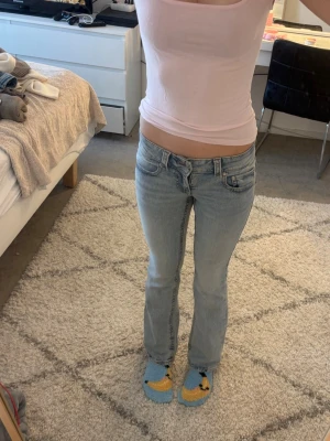 Ljusblå gina jeans - Säljer ett par ljusblå bootcut jeans med låg midja. Jeansen har en snygg tvätt och raka ben som går ut lite nedtill. Perfekta till en avslappnad och trendig look. Fickorna har knappar som går att öppna.
