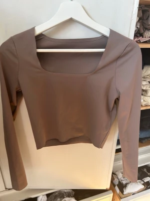 Brun croppad topp - Snygg brun croppad topp från ICANIWILL med lång ärm och fyrkantig urringning. Perfekt att ha till vardags men går också att träna med. Säljer då jag känner att den behöver ett nytt hem.