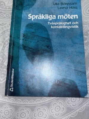 Språkliga möten kursbok - Kursbok 'Språkliga möten: Tvåspråkighet och kontaktlingvistik' av Ulla Börestam och Leena Huss. Boken har ett blått omslag med abstrakt mönster och är tryckt på vanligt papper. Perfekt för dig som pluggar språkvetenskap eller lingvistik.