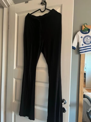 Svarta mjukisbyxor från SHEIN - Säljer ett par svarta mjukisbyxor från SHEIN med utsvängda ben och dragsko i midjan. Byxorna är i mjukt och stretchigt material, perfekta för chill dagar. Klassisk svart färg som passar till allt och enkel att matcha med olika toppar.