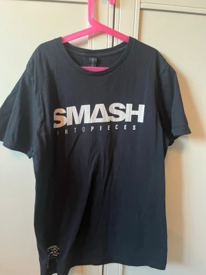 Svart Smash Into Pieces t-shirt - Cool svart t-shirt från Smash Into Pieces med stort vitt tryck på bröstet och en snygg patch på ärmen. Klassisk passform och rund halsringning, perfekt för dig som gillar bandmerch och streetstyle. Har en exakt likadan som också är till salu!