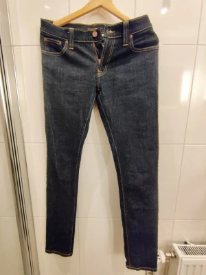 Nudie Jeans - Tight Long John - W29 L32 - Snygga mörkblå skinny jeans från Nudie Jeans med klassisk femficksmodell och kontrastsömmar i gult. Jeansen har dragkedjegylf och är tillverkade i kraftigt denimtyg. Perfekta för dig som gillar en slimmad passform och stilren look. Storlek W29 L32. Modell Tight Long John.