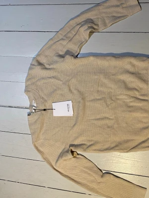 Beige stickad tröja Selected Homme - Säljer en beige stickad tröja från Selected Homme i ekologisk bomull. Tröjan har rund halsringning, ribbade muddar och en diskret struktur i materialet. Perfekt för dig som gillar stilrena och enkla plagg. Nypris: 499