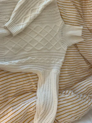 Vit polotröja med flätstickat mönster - Säljer en krämvit stickad polotröja med snyggt flätmönster och ribbade muddar. Tröjan har hög polokrage och är gjord i mjukt material, perfekt för kyliga dagar. Passar dig som gillar klassisk och mysig stil.