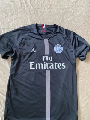 Psg t-shirt - Passar M och L .Säljer en svart PSG matchtröja med Fly Emirates-tryck på bröstet och Paris Saint-Germain-logga. Tröjan har korta ärmar, grå vertikal rand framtill och siffran 10. Tillverkad i ett lätt och ventilerande material