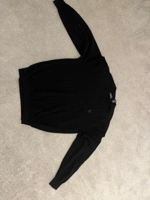 Svart stickad tröja från Ralph lauren Chaps - Klassisk svart stickad tröja från Chaps i 100% bomull. Tröjan har rund halsringning, långa ärmar och diskret logga på bröstet. Perfekt för lager på lager och enkel att matcha med olika outfits.
