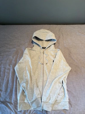 Ralph lauren zip - Säljer en ljusgrå Ralph lauren zip hoodie med dragkedja och huva. Hoodien har dragsko i huvan, ribbade muddar vid ärmslut och nederkant samt fickor på sidorna. Perfekt för en avslappnad och chill stil. Materialet känns mjukt och bekvämt.