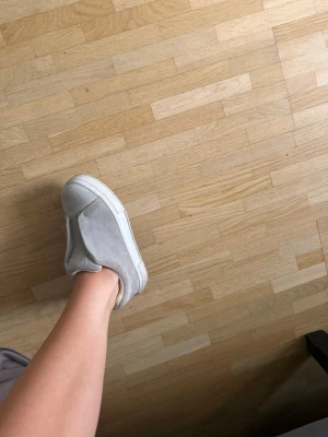 Grå slip-on sneakers i mocka - Säljer mina snygga EYTYS grå slip-on sneakers i mocka med vit sula. Skorna har en minimalistisk design utan snörning och en låg profil som gör dem enkla att ta på. Perfekta för en clean och avslappnad stil.köpta för 1900kr 