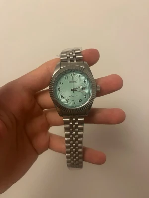 Seiko Mod light blue dial - Stilren Seiko automatisk klocka med ljusblå urtavla och klassisk länk i silverfärgat metall. Urtavlan har tydliga siffror och markerade index, samt räfflad boettkant som ger en cool touch. Perfekt accessoar för dig som gillar tidlös design.