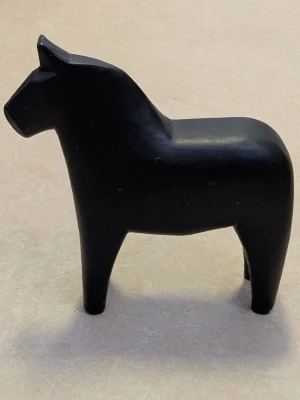 Svart dalahäst i trä - En stilren svart dalahäst i trä med klassisk form. Perfekt som dekoration i hemmet eller som en svensk souvenir. Hästen har en matt finish och är handgjord med mjuka linjer. Höjd ca 15 cm