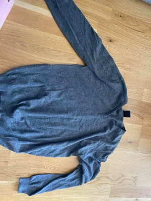 Grå stickad tröja från SMOG - Mysig grå stickad tröja från SMOG i regular fit. Tröjan har långa ärmar, rund halsringning och är tillverkad i ett mjukt material som passar perfekt till kyligare dagar. Enkel och stilren design som funkar till det mesta.