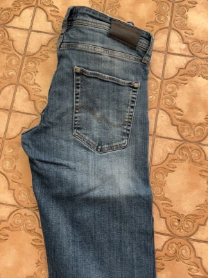 Blå raka jeans från Jack and Jones  Jeans - Snygga blå jeans från jack and Jones  Jeans med klassisk femficksmodell och raka ben. Jeansen har en diskret slitning och kontrastsömmar på bakfickan. Tillverkade i mjuk denim som ger en avslappnad look. Tapered/Mike