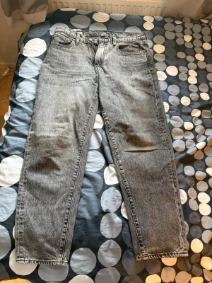 Grå Levi's 562 jeans straight fit - Säljer ett par klassiska grå Levi's 562 jeans med rak passform och fem fickor. Jeansen har en snygg tvättad look, knappgylf och den ikoniska läderlappen bak i midjan. Perfekta för dig som gillar vintage vibe och tidlös stil.