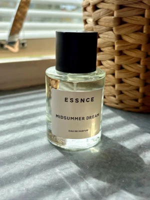 ESSNCE Midsummer Dream parfym - Fräsch parfym från ESSNCE med namnet Midsummer Dream. Flaskan är genomskinlig med en enkel vit etikett och svart text, samt ett stilrent svart lock. Doften är en Eau de Parfum och flaskan har en modern, rund form. Ny