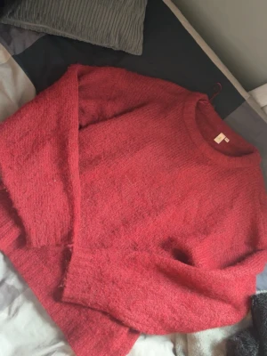 Röd fluffig stickad tröja från Nelly - Mysig röd stickad tröja från Nelly i fluffigt material. Tröjan har rund halsringning och långa ärmar, perfekt för kyliga dagar. Enkel och stilren design som passar till det mesta.