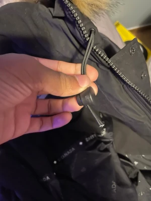 Svart parkas från Zavetti Canada - Snygg svart parkas från Zavetti Canada med dragkedja, justerbar dragsko och fuskpäls vid huvan. Jackan har ett stort broderat märke med röd lönnlöv på ärmen och är fodrad för extra värme. Perfekt för kalla dagar och riktigt stilren.