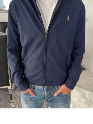 Marinblå jacka från Polo Ralph Lauren - Snygg marinblå jacka från Polo Ralph Lauren med dragkedja framtill och diskret logga på bröstet. Jackan har ribbade muddar vid ärmslut och midja samt klassisk krage. Perfekt till jeans och t-shirt för en clean look. Har använt 2 gånger då jag testade den men inte min stil, ORDINARE PRIS ca:3000kr  MITT PRIS 1799!!! skriv vid intresse!😊👍