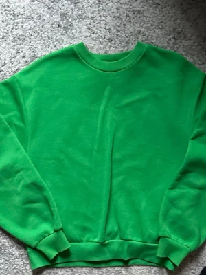 Grön crewneck sweatshirt - En enkel och stilren grön crewneck sweatshirt med rund hals och ribbade muddar vid ärmslut och nederkant. Perfekt för dig som gillar en clean look och vill ha något bekvämt till vardags. Materialet känns mjukt och skönt mot huden.