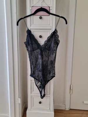Svart spetsbody med tunna axelband från Zara strl S - Säljer en svart, transparent spetsbody med djup V-ringning och tunna axelband. Bodyn har ett blommigt spetsmönster och scallop-kant längs urringningen. Perfekt för dig som gillar en feminin och elegant look. Är från Zara i storlek S. Aldrig använd men tvättad efter köp. 